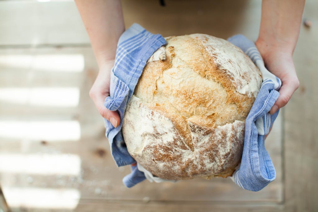 Close-up of artisan bread held in hands with a blue cloth on a wooden table.