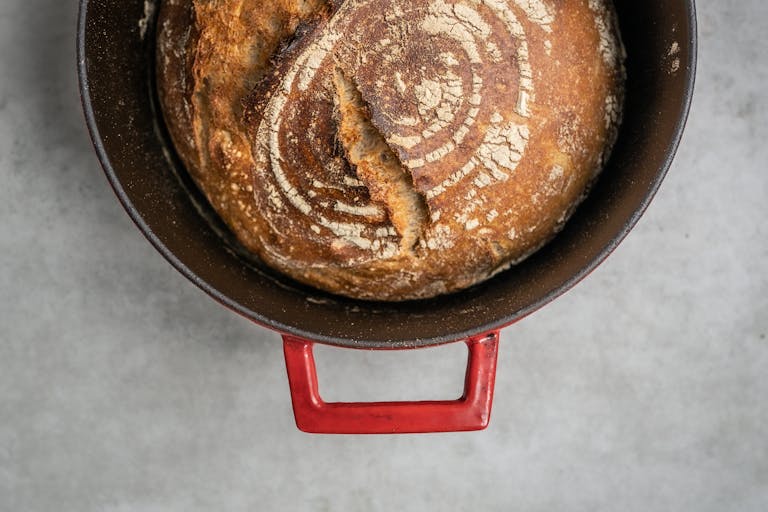 Freshly baked artisan bread in a red Dutch oven, showcasing rustic texture.