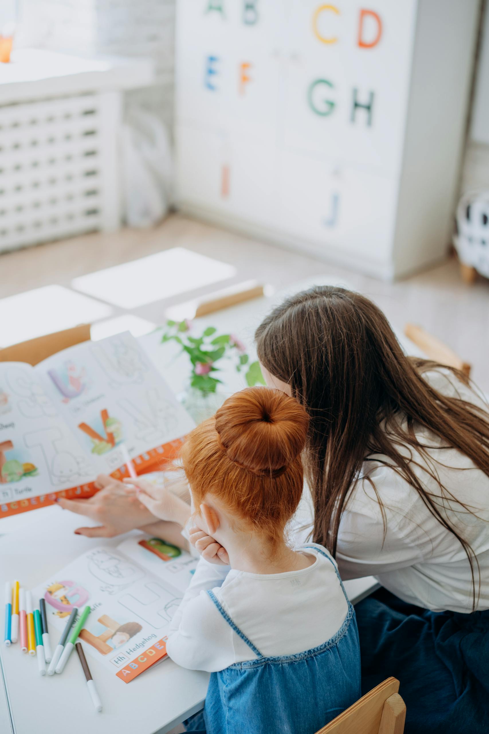 A woman helps her daughter with homework at a desk, emphasizing education and bonding.