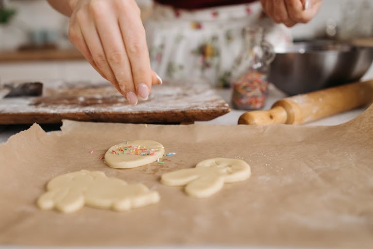 Close-up of person decorating cookies with sprinkles on parchment paper.