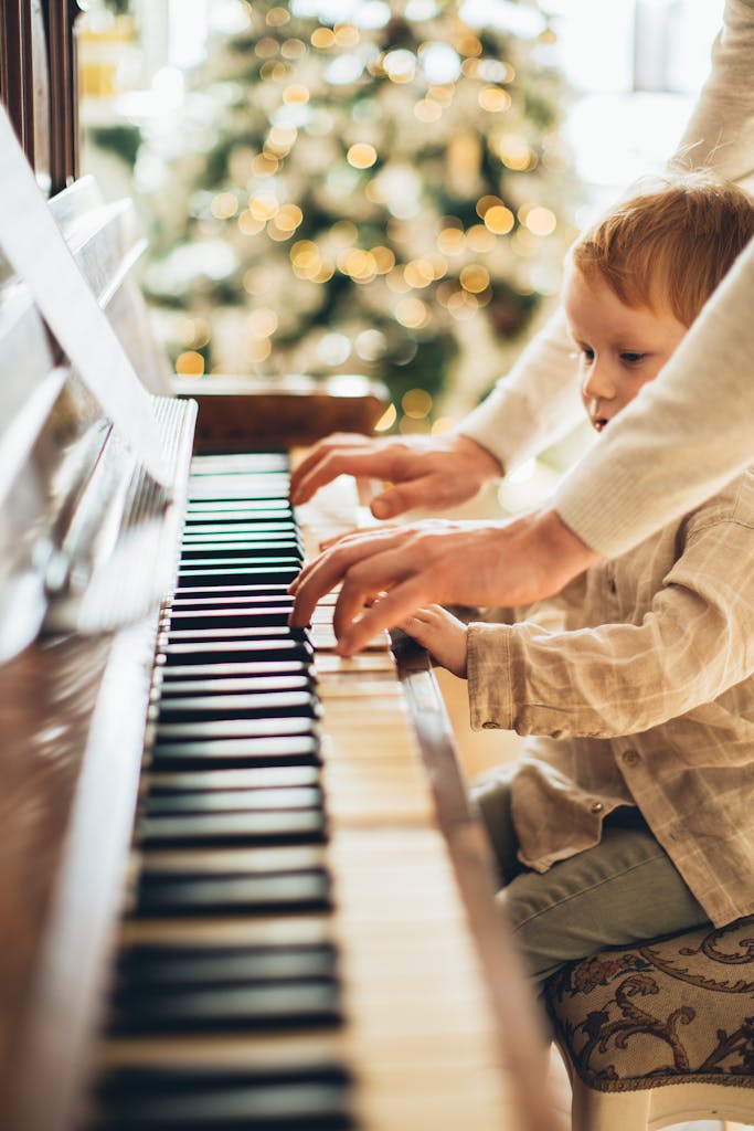 A child and adult play piano together near a decorated Christmas tree, creating a warm holiday atmosphere.