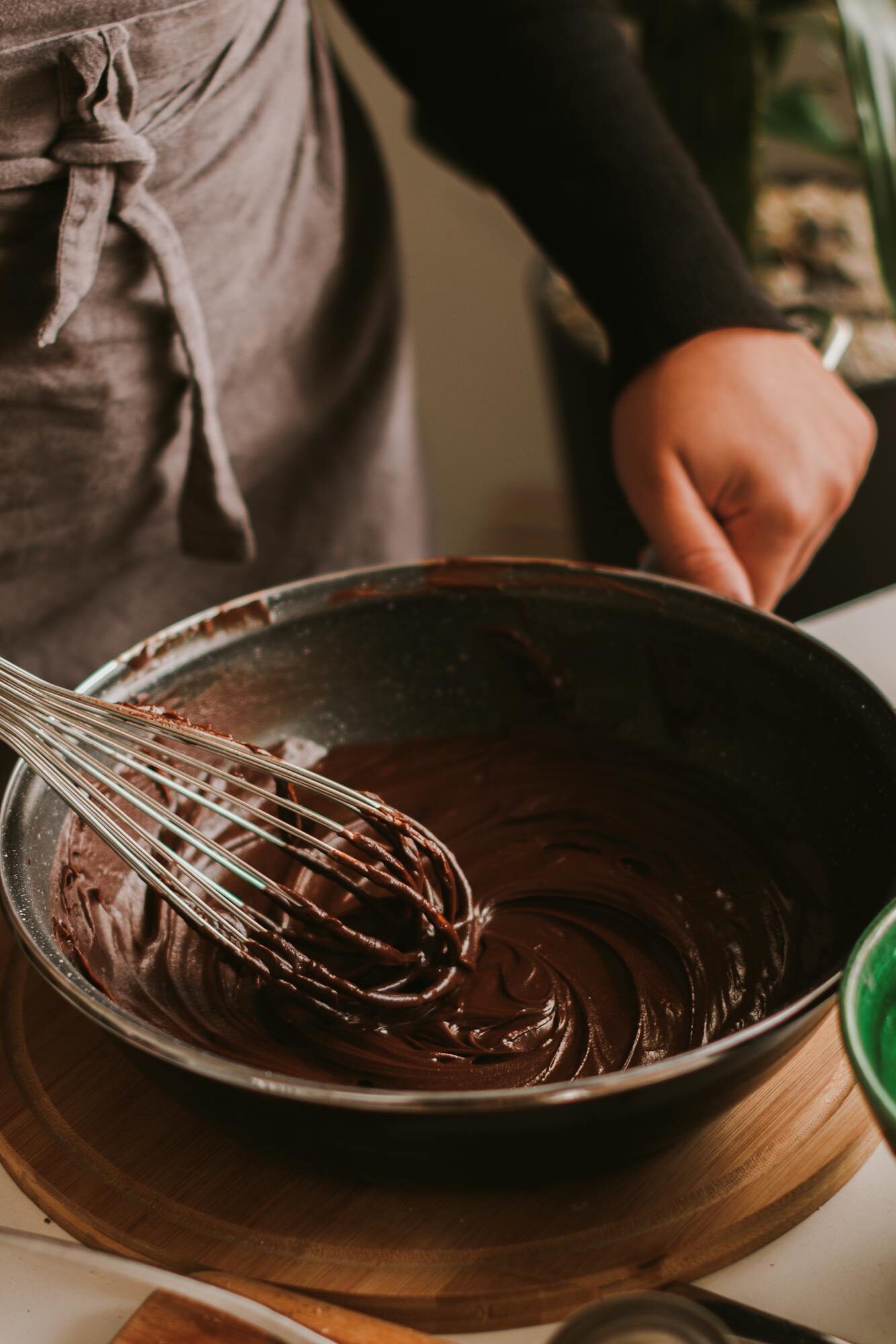 A person whisking rich chocolate batter in a cozy kitchen setting.