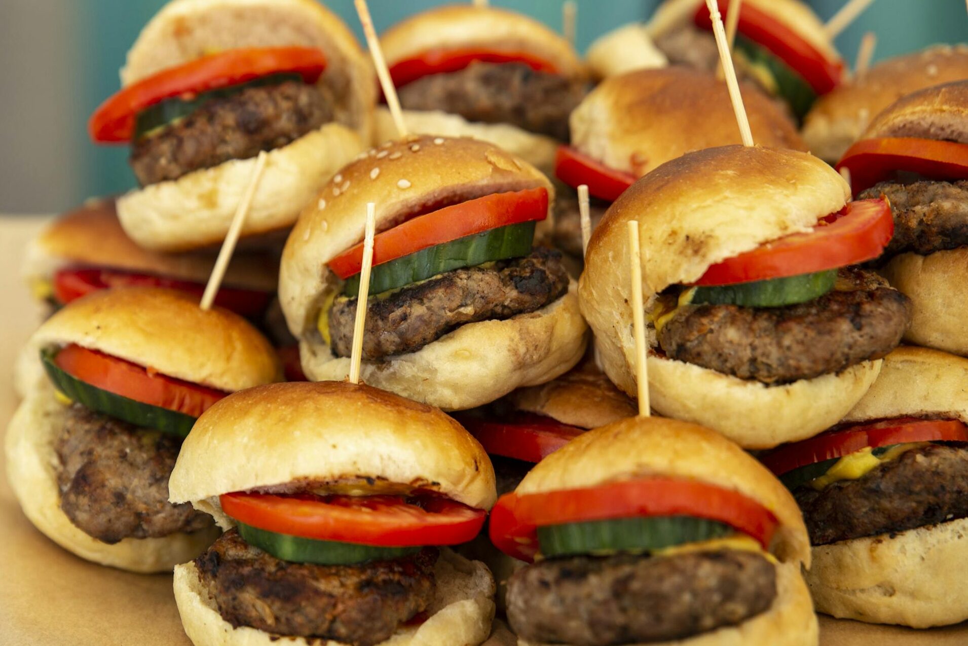 A tempting platter of mini burgers with fresh tomatoes and cucumbers, perfect for any gathering.