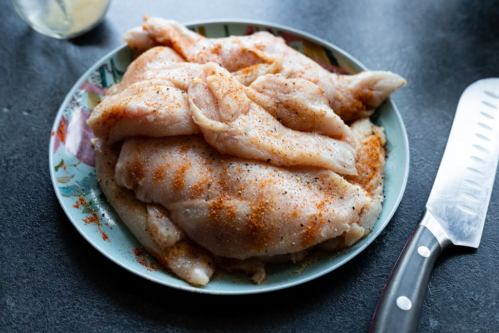 Close-up of seasoned raw chicken breasts on a colorful plate next to a sharp kitchen knife.