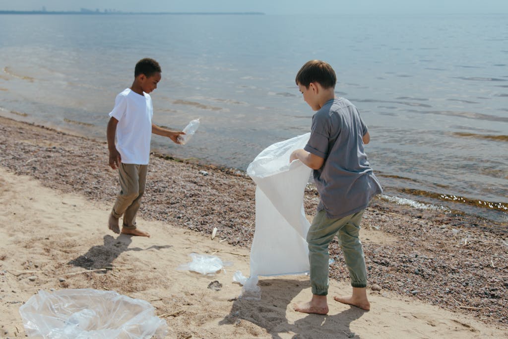 Two boys collect garbage at the beach, promoting volunteerism and environmental care.
