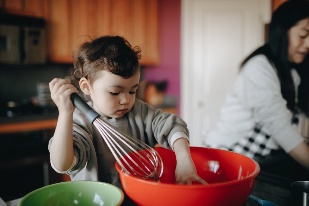 Young child assisting in the kitchen with a large red mixing bowl, showcasing curiosity and bonding time.