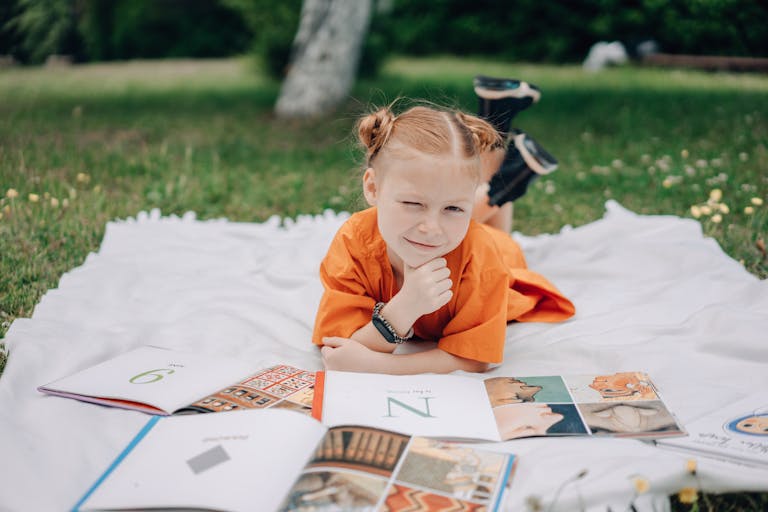 Cheerful child enjoying a book outdoors on a sunny day, showcasing learning and relaxation.