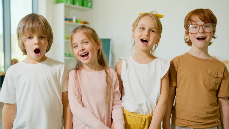 Group of cheerful children smiling and singing in a bright classroom setting.