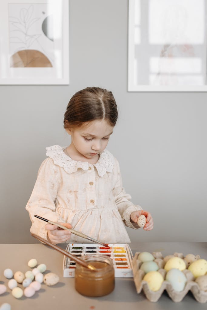 Little girl painting eggs with watercolors indoors, perfect for Easter celebration themes.