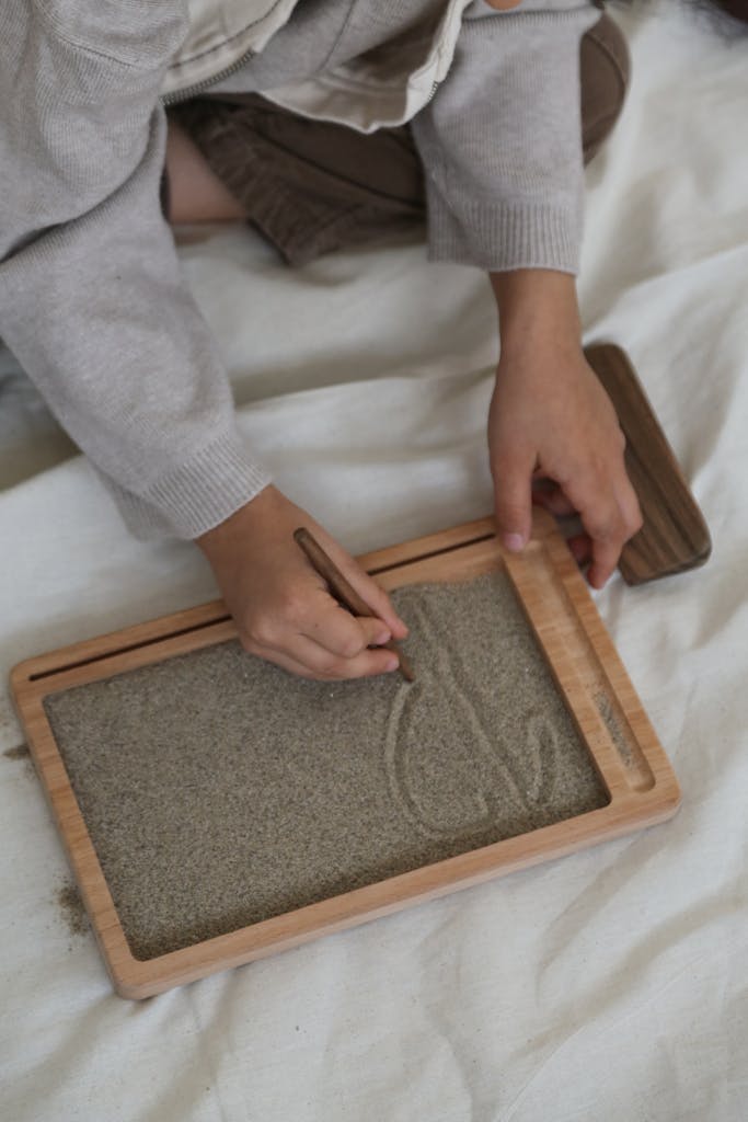 A child practicing writing skills using a Montessori sand tray indoors.