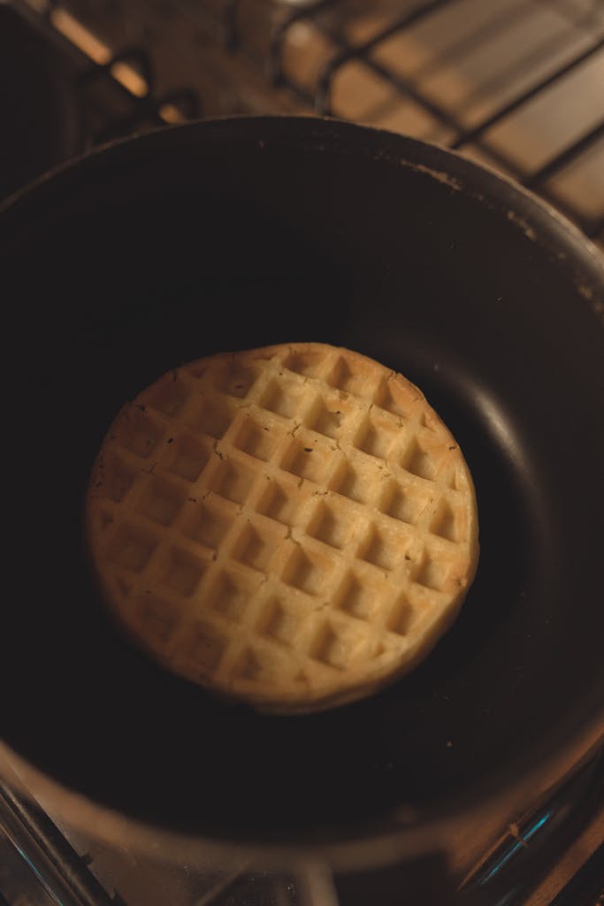 A single waffle being cooked in a frying pan on a stove in a kitchen setting.