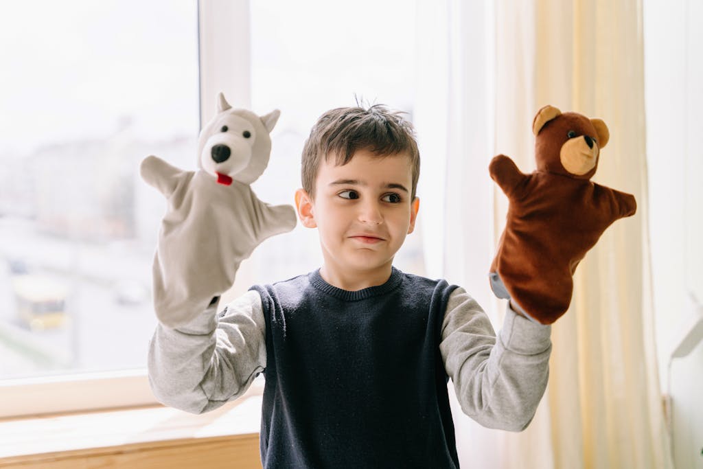A young boy joyfully plays with bear and polar bear hand puppets indoors. Bright daylight setting.