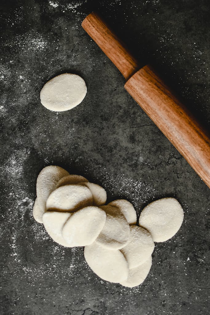 Overhead shot of raw dough circles and a wooden rolling pin on a floured surface.