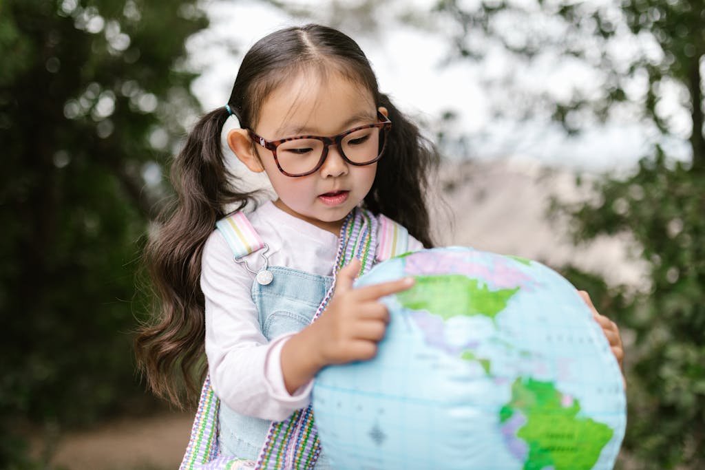 Curious child with glasses points to a globe outdoors, learning geography.