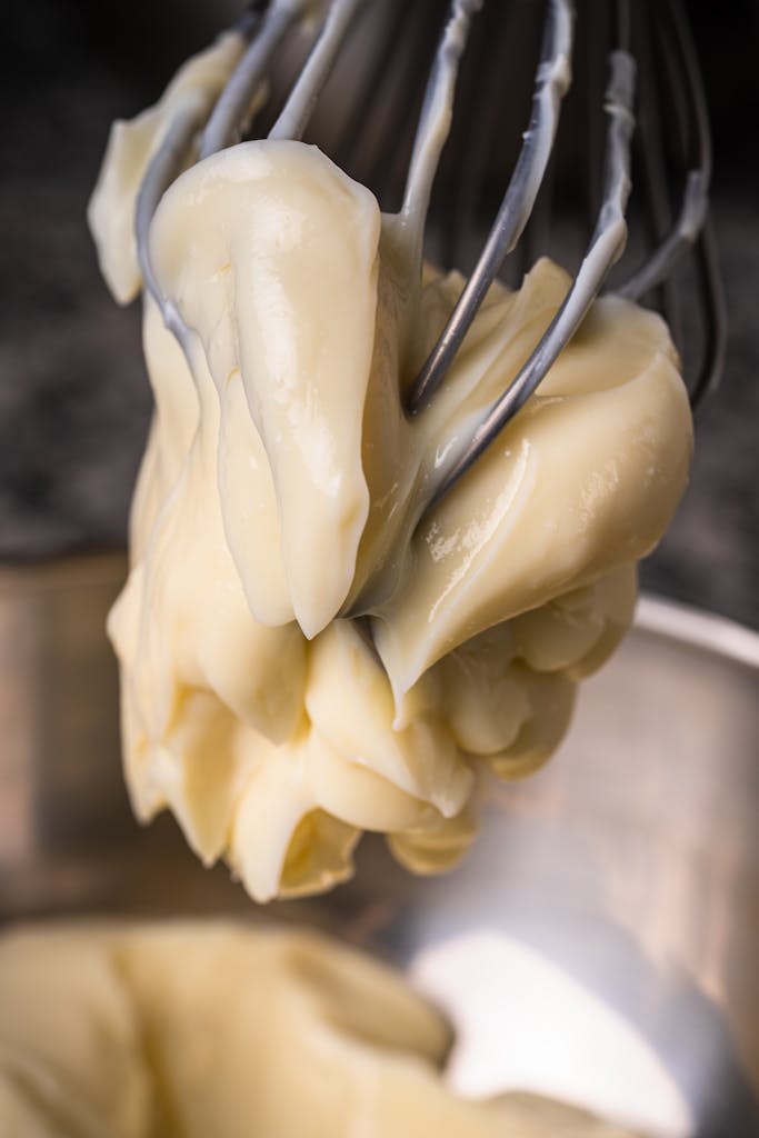 Detailed close-up of a creamy dough mixture on a whisk over a metallic mixing bowl.