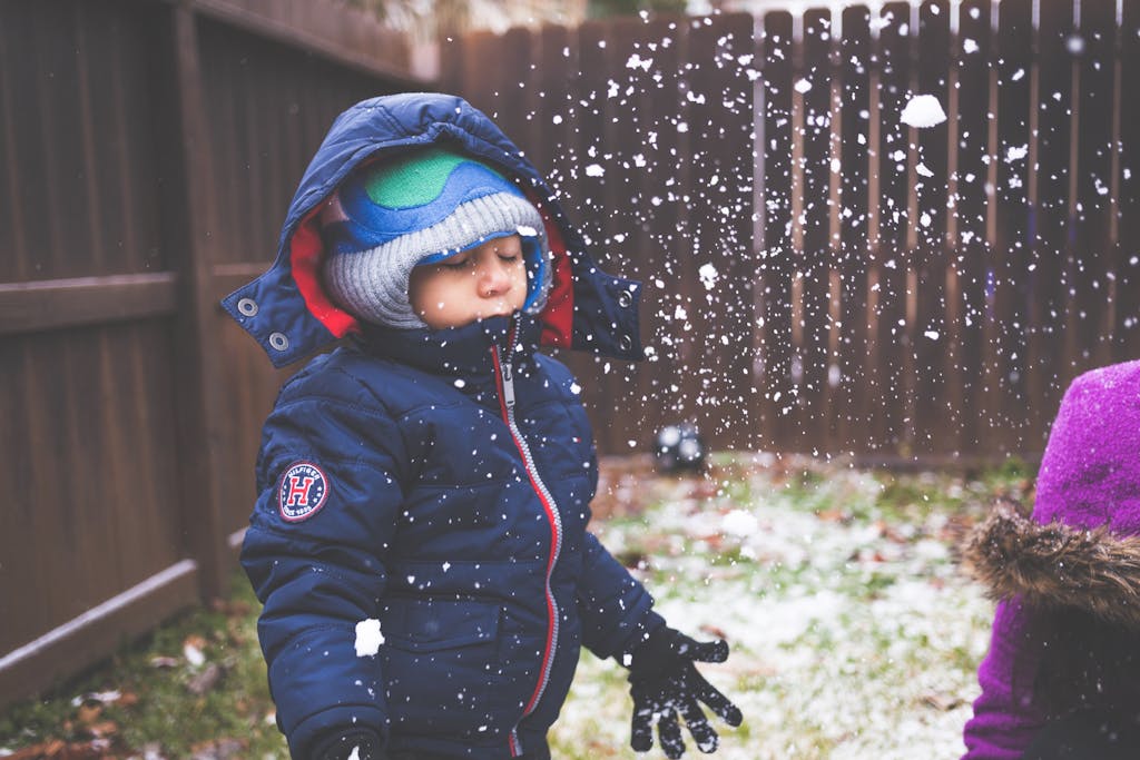 A young child dressed warmly enjoying a snowy winter day in a backyard.
