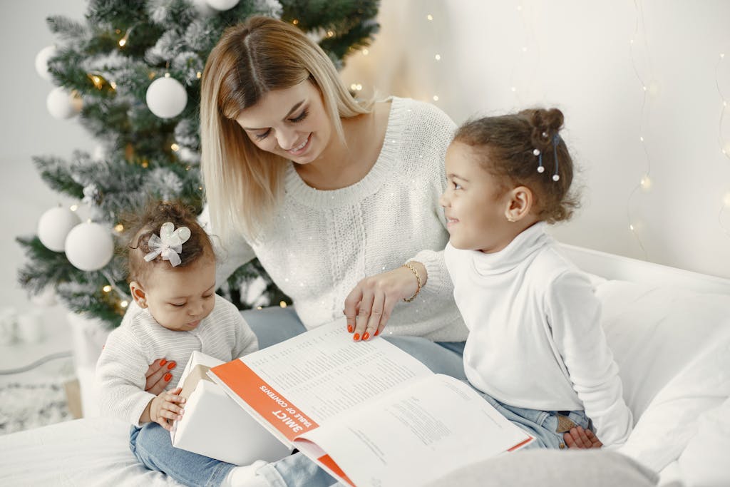 A joyful family moment with a mother and daughters reading together near a Christmas tree.