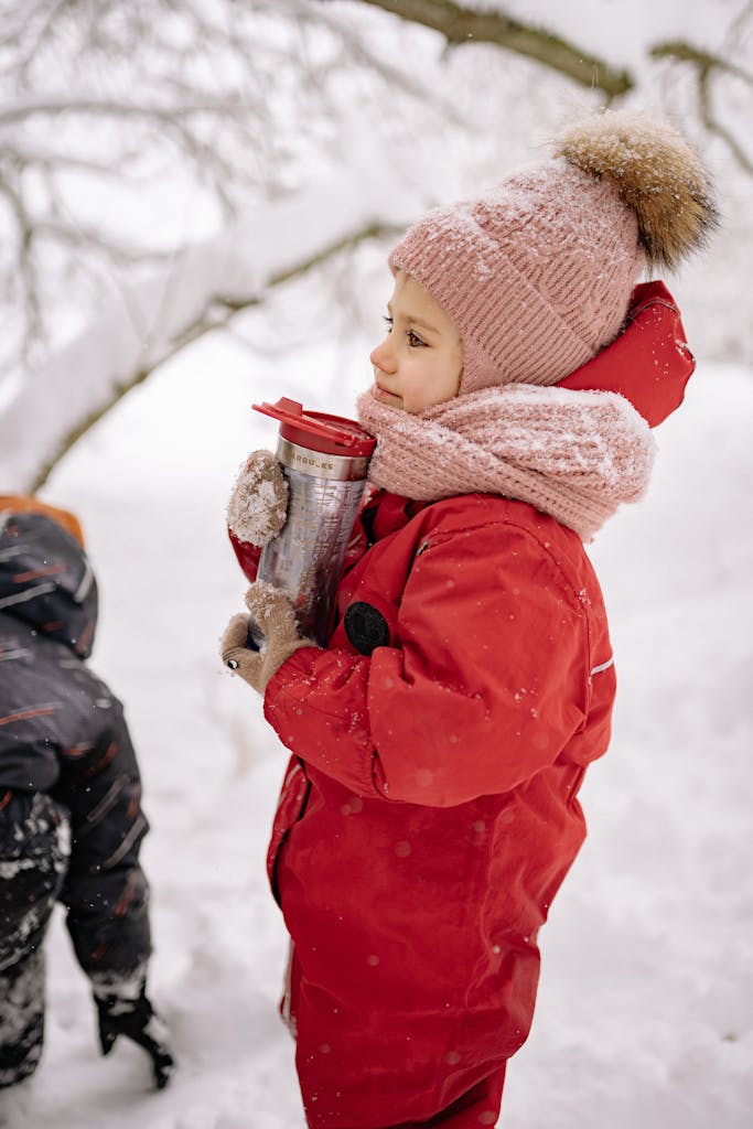 A child warmly dressed in red clothing holds a drink while enjoying the snowy winter outdoors.