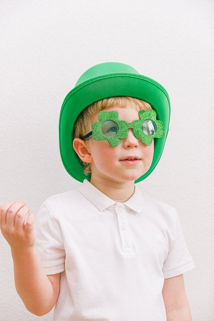 Cute child in green outfit celebrating Saint Patrick's Day with clover glasses.